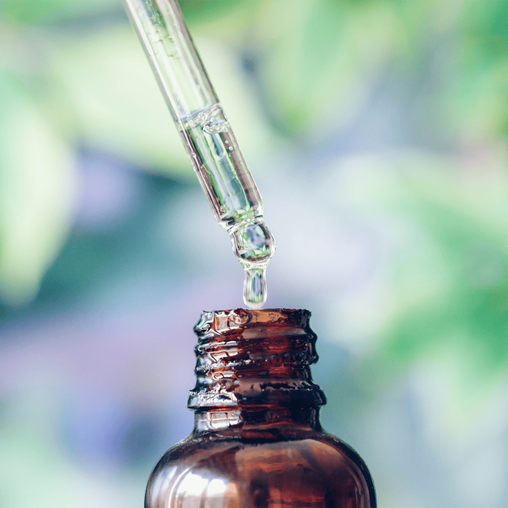 Hemp Products That Are Still Allowed In Texas After Recent Ban - Modern CBD & Wellness - Modern CBD & Wellness Close-up of a glass dropper releasing liquid into the neck of a brown glass bottle, with a soft green background.